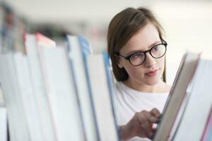 porträtt av famale studerande väljer bok till läsa i bibliotek foto