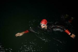 triathlon idrottare simmar i mörk natt iklädd våtdräkt foto