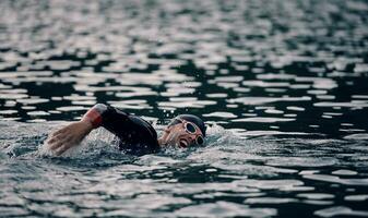 triathlon idrottare simmar på sjön i soluppgången bär våtdräkt foto