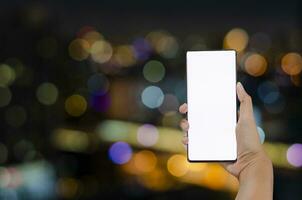 män eller kvinnor händer innehav på smartphone tom vit skärm på natt färgrik bokeh bakgrund. kopia Plats inmatning text foto