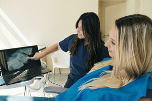 kvinna ortodontist förklara ung kvinna röntgen bild på bärbar dator foto