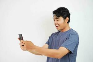 upphetsad leende eller Lycklig ung asiatisk man i Marin Färg t-shirt innehav telefon, isolerat på vit bakgrund foto