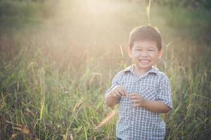 glad liten asiatisk pojke som leker utomhus. söt asiatisk. pojke på fältet. foto