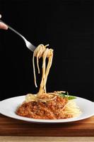 hand som håller en gaffel med spaghetti och röd sås i vitt fat foto