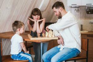 Lycklig familj mor, pappa och deras son spelar schack i de rum foto