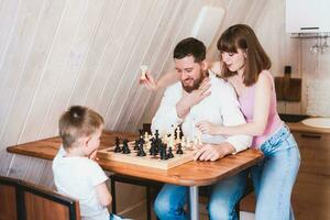gravid mamma tittar på pappa och son spela schack på de tabell foto