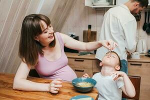 Lycklig barn äter pasta i de kök med henne familj foto
