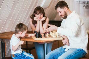 Lycklig familj mor, pappa och deras son spelar schack i de rum foto