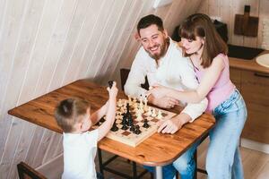 gravid mamma tittar på pappa och son spela schack på de tabell foto