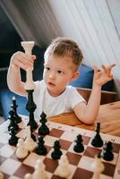 liten pojke spelar schack på Hem på de tabell foto