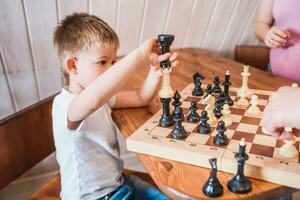 liten pojke spelar schack på Hem på de tabell foto