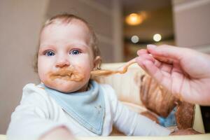 Lycklig mor matning henne söt liten dotter frukt puré från en sked. först mat foto