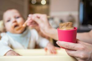 Lycklig mor matning henne söt liten dotter frukt puré från en sked. först mat foto