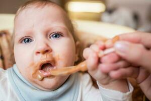 mamma matar henne liten dotter frukt puré från en sked. först mat foto