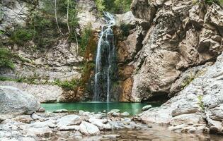 underbar små vattenfall den där former en damm av smaragd- vatten i en skog foto