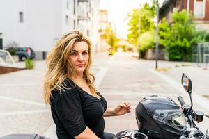 porträtt av blond mogna kvinna med cyklist hjälm Sammanträde på motorcykel utomhus foto