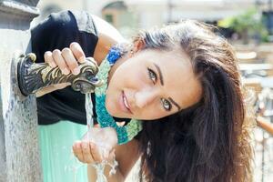 porträtt av Söt flicka drycker vatten från källa i sommar stad foto