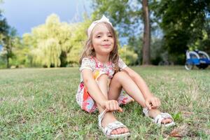 porträtt av söt flicka med en papper krona Sammanträde i en offentlig parkera foto