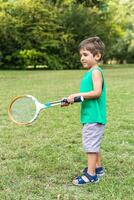 leende söt barn spelar med ett gammal tennis racket i en offentlig parkera foto