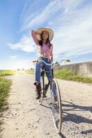 Söt ung kvinna på cykel i en Land väg foto