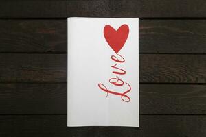 valentines kort. vit papper kort med röd hjärta och inskrift kärlek. foto