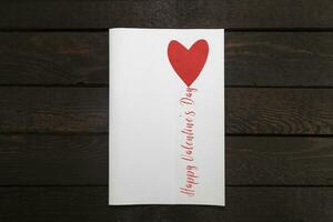 valentines kort. vit papper kort med röd hjärta och inskrift Lycklig hjärtans dag. foto