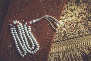de helig quran med radband och bön- matta. bild av de helig quran med radband. muslim radband pärlor och koranen. platt lägga se foto