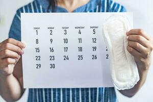 kvinna innehav en gång i månaden kalender och sanitär dynor. menstruation cykel kalender. kvinnor hälsa begrepp. period dagar begrepp som visar feminin menstruations- cykel. foto