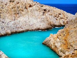 Fantastisk ljus blå vatten i en avskild cove med orange klippor omgivande den - Kreta, grekland foto