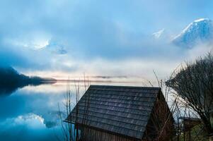 små trä- hus på de gräns av de sjö med dimmig bergen på de bakgrund foto