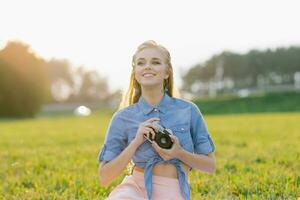 studerande flicka innehar en kamera i henne händer i de sommar utomhus foto