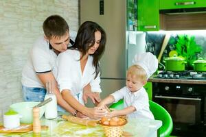 Lycklig familj mamma och liten son och pappa är framställning deg i kök på tabell. Produkter för deg är på tabell foto