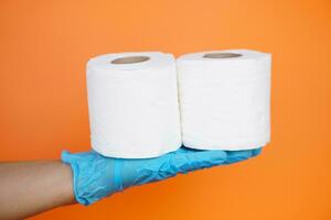 stänga upp hand innehar rulla av vit vävnad papper, isolerat på orange bakgrund. begrepp, rengöring verktyg, hygienisk till torka smutsig och absorbera våt ,använda sig av vävnad papper för hygienisk och sanitär.toalett papper foto
