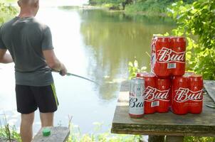 budweiser knopp öl burkar packa på gammal tabell och fiskare på flod på bakgrund foto