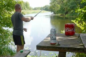 budweiser knopp öl burkar packa på gammal tabell och fiskare på flod på bakgrund foto