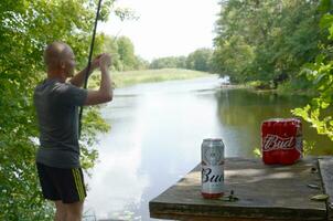 budweiser knopp öl burkar packa på gammal tabell och fiskare på flod på bakgrund foto