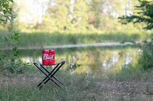 budweiser knopp öl burkar packa på hopfällbar stol utomhus på de flod och grön träd bakgrund foto