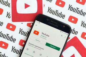 Youtube app på samsung smartphone skärm på papper baner med små Youtube logotyper och inskriptioner. Youtube är Google dotterföretag och amerikan mest populär videodelning plattform foto