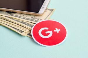 Google plus papper logotyp lögner med kuvert full av dollar räkningar och smartphone foto