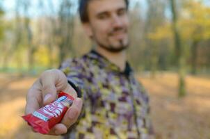 Kharkov, ukraina - oktober 21, 2019 ung man passerar en utrustning kat choklad bar i ett höst parkera. de manifestation av vänlighet, behandla med sötsaker foto