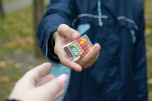 Kharkov, ukraina - oktober 26, 2019 ung man tar tic tac paket till flicka i höst parkera. tic tac är populär på grund av dess mynta färsk smak förbi ferrero foto