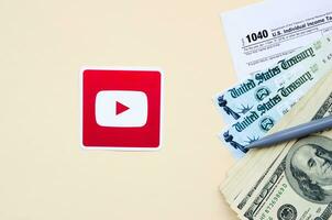 Youtube tryckt logotyp lögner med 1040 enskild inkomst beskatta lämna tillbaka form med återbetalning kolla upp och hundra dollar räkningar på beige bakgrund. hjälp i beskatta period från social nätverk begrepp foto