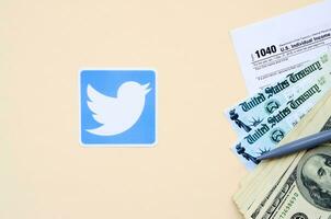 Twitter tryckt logotyp lögner med 1040 enskild inkomst beskatta lämna tillbaka form med återbetalning kolla upp och hundra dollar räkningar på beige bakgrund. hjälp i beskatta period från social nätverk begrepp foto