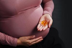 närbild gravid kvinna som håller medicin på svart bakgrund foto