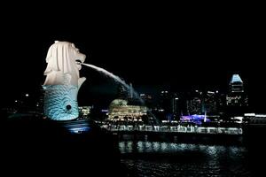 singapore, augusti 20, 2023- sida se av merlion besprutning de vatten med stadsbild på natt och sjö i bakgrund foto