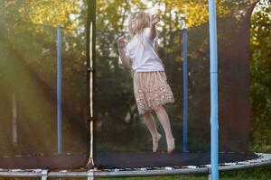 liten barn flicka Hoppar på de trampolin i de tillbaka gård foto