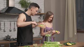 muskulöst ungt par som lagar hälsosam cocktail efter träning, pratar och skrattar i köket. sport, kost, hälsosam mat koncept, slow motion foto