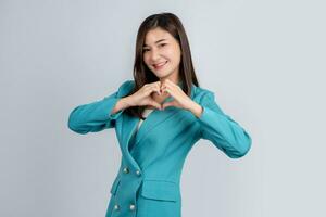 Lycklig asiatisk företag kvinna i ljus grön kostym som visar hjärta tecken med händer isolerat på vit bakgrund foto