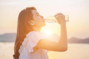 vacker ung kvinna som dricker vatten med soluppgången på morgonen foto