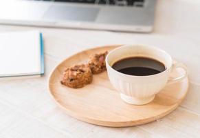 svart kaffe och kakor med bärbar dator och anteckningsbok på bordet foto